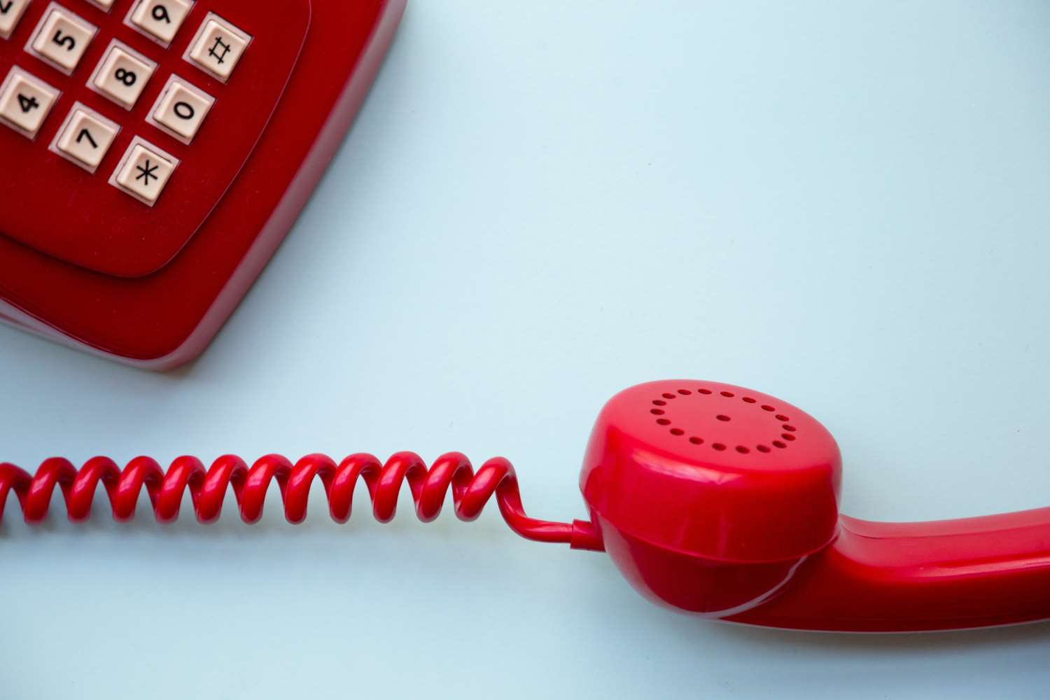 Close-up of a red vintage telephone with coiled cord on a light background.